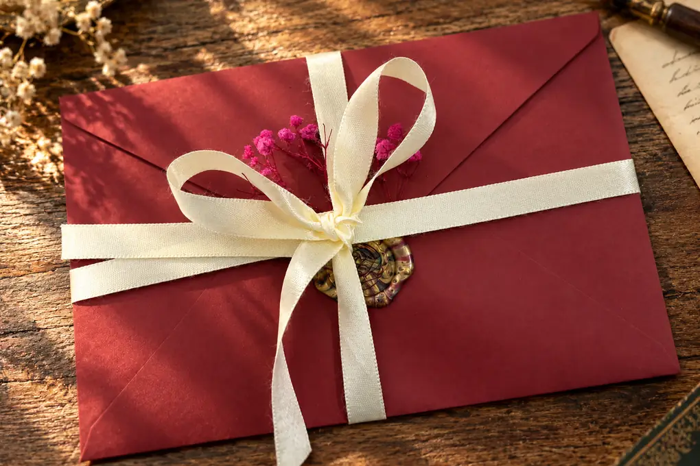 A deep red envelope tied with a cream ribbon bow