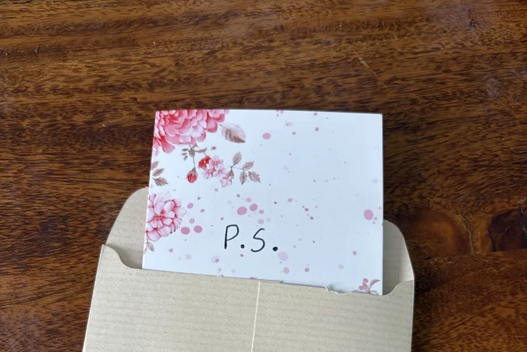 A P.S. card being tucked into a kraft envelope