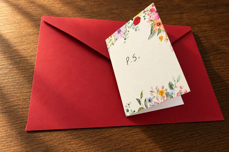 A handwritten P.S. card resting on one of our envelopes